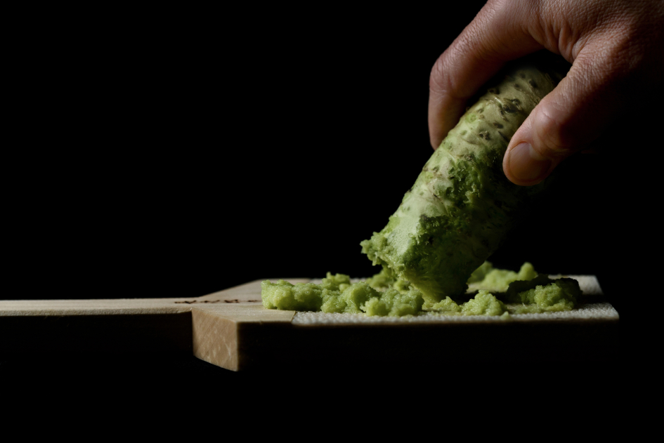 A hand holding a wasabi root against the grater.